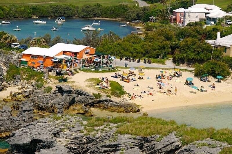 A small beach, a café and boats at anchor in a bay, seen from a headland