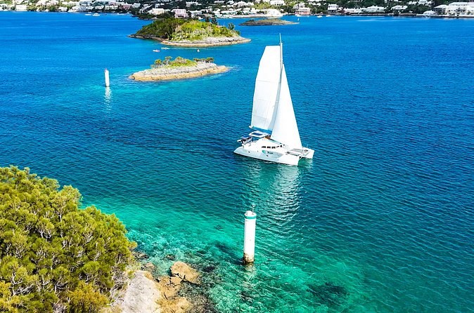 A white catamaran sailing between small green islands, seen from above