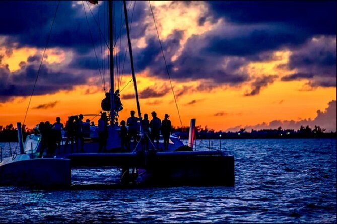 A catamaran in silhouette under an orange sunset sky
