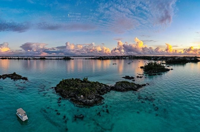 Small rocky islets and a boat in calm water under a pink sky, from the air