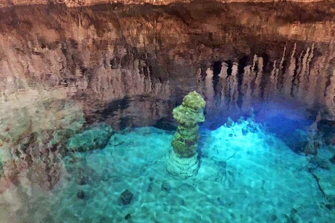 A column of rock rising from a lit blue pool inside a cave
