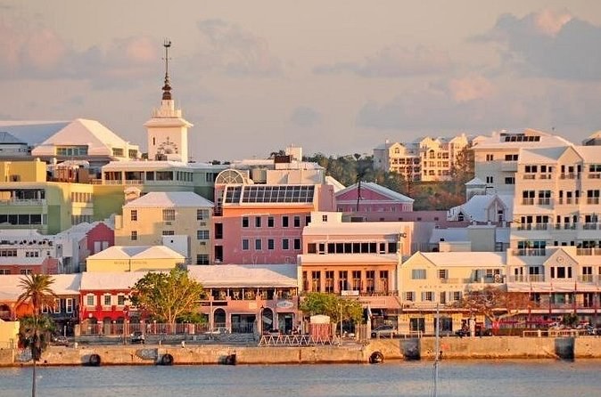 Pastel buildings and a white clock tower above a harbour front at dusk