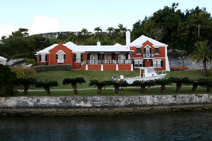 A red house with a stepped white roof on a lawn at the water's edge