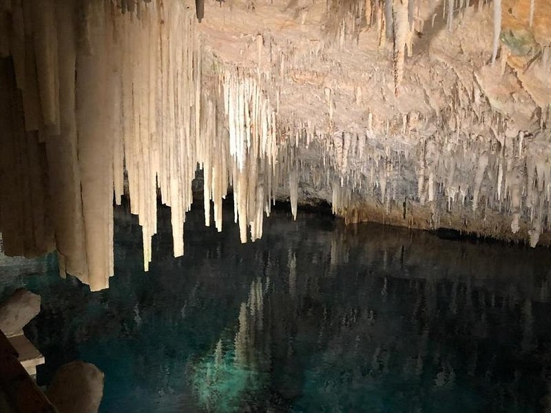 Pale stalactites hanging over the still water of a cave lake