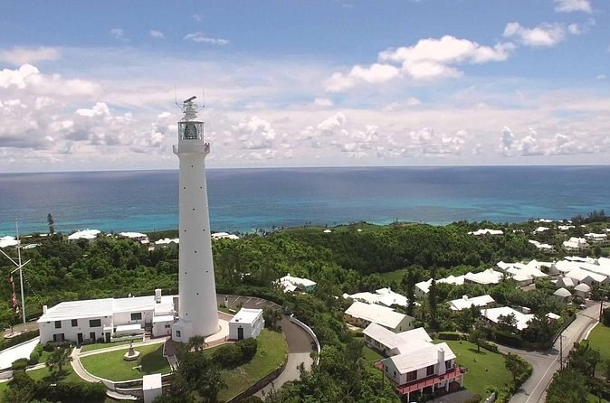 A tall white lighthouse on a green hill above white roofs and the open sea